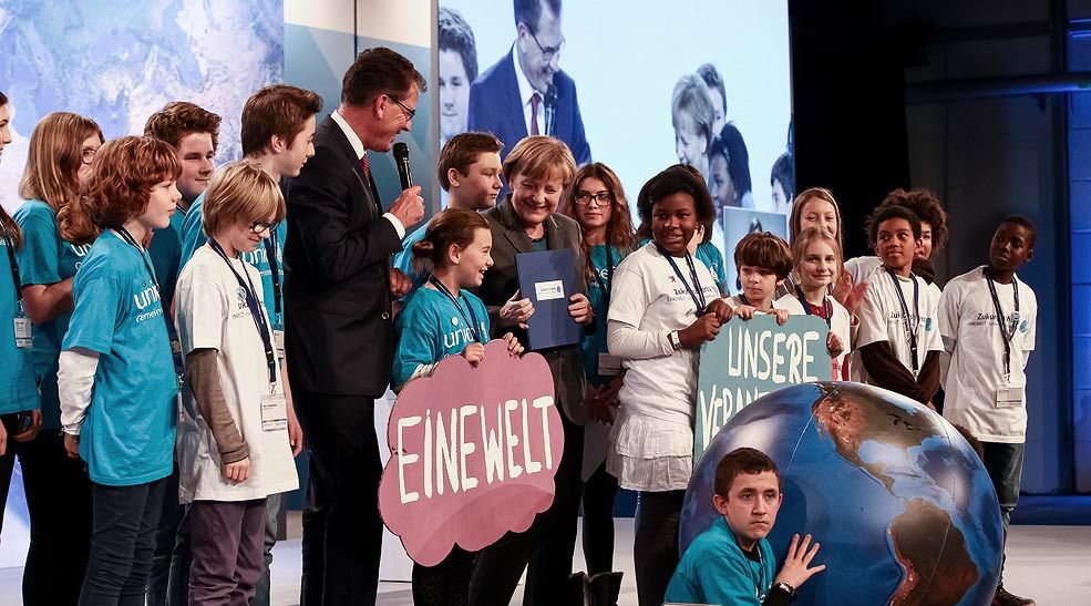 Bundeskanzlerin Angela Merkel, Minister Müller (BMZ) und Schülerinnen und Schüler stehen gemeinsam auf der Bühne. Foto: Andreas Lemke Photography. www.andreaslemke.com