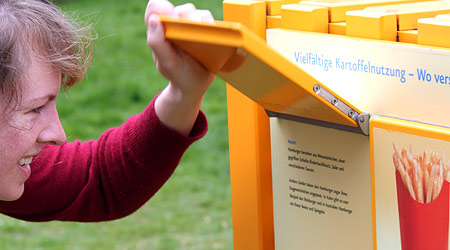 Eine Besucherin des Weltgartens liest den Text hinter der Klappe einer Informationstafel. Foto: Peter Wattendorf